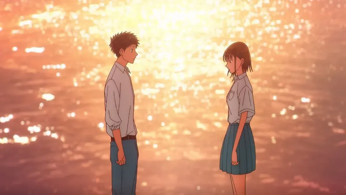 A boy and a girl in school uniforms stand facing each other at the water's edge while the sea glitters orange at sunset, in a still from Blue Box